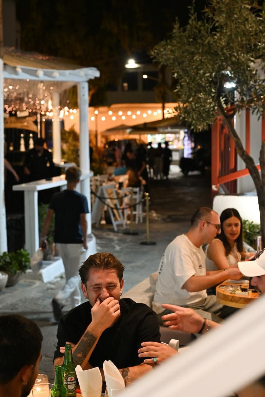 The lively Lakka square in Mykonos Old Town at night, strung with lights around an olive tree.
